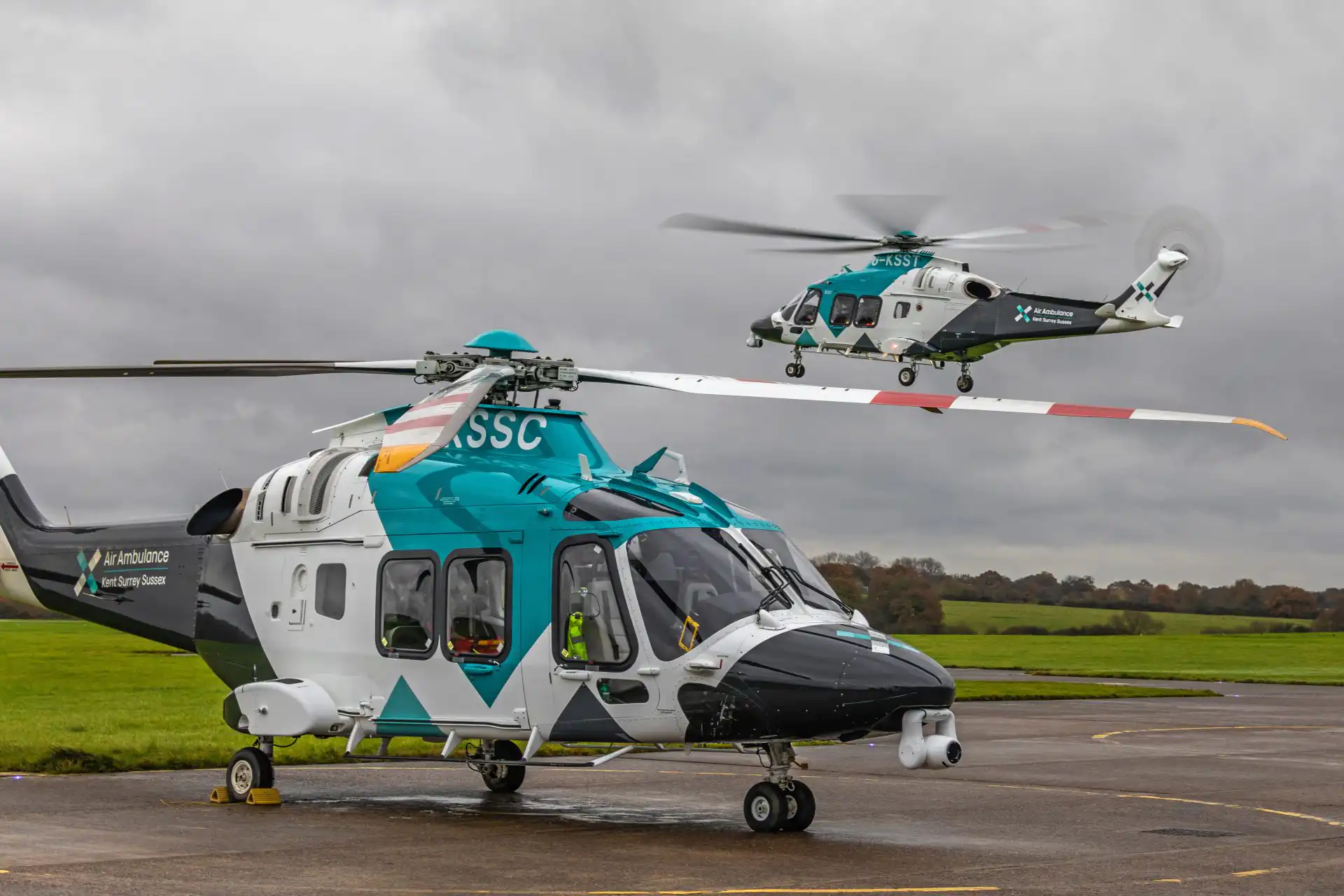 Two helicopters, one on the ground and one behind it in the air
