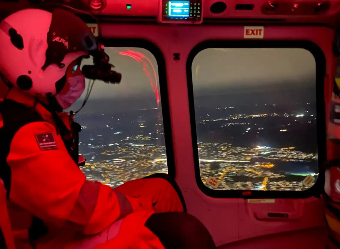 Crew member wearing night vision goggles looking out of the aircraft at night