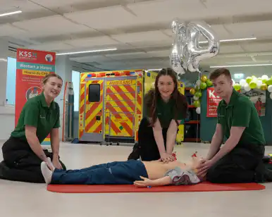 Three student paramedics kneeling by a mannikin as one performs CPR.