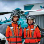 2 crew standing in front of the air ambulance helicopter.