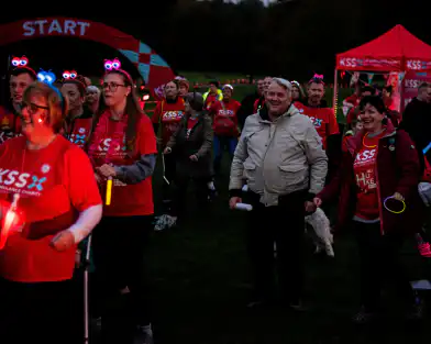 Group of walkers taking part in charity walk at night wearing glowing accessories