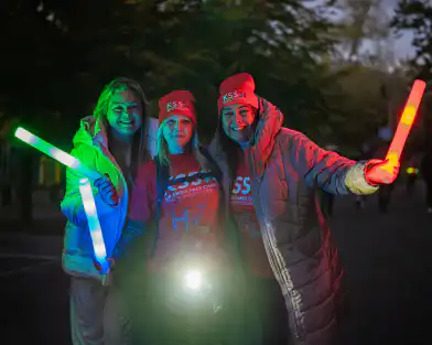 Three people in warm clothing at night holding glow sticks