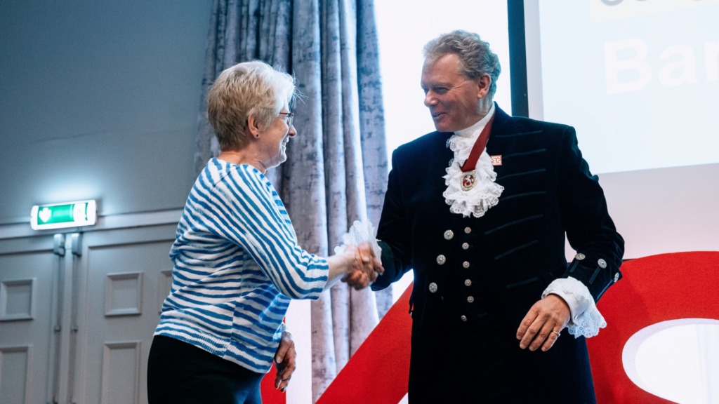 Woman in striped top shaking hands with man wearing ceremonial clothes