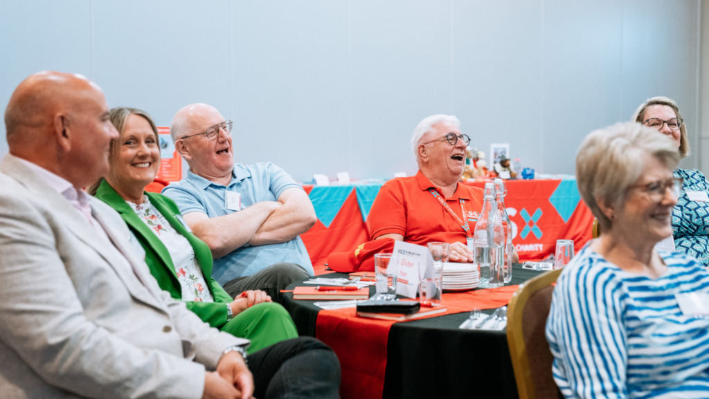 Small group of seated people, laughing and smiling looking to the right.