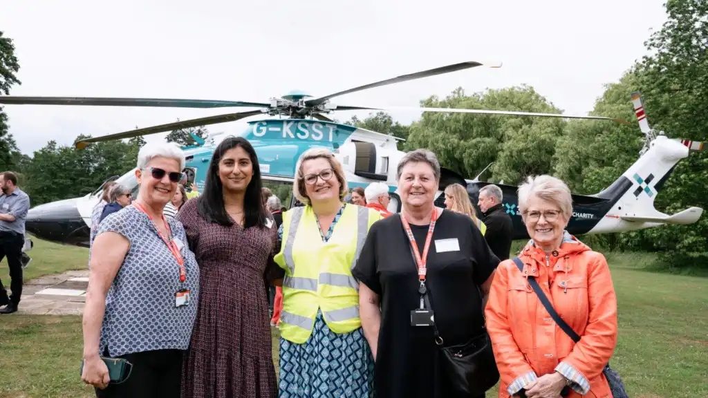 Group of five women smiling facing camera with helicopter on the ground in the background