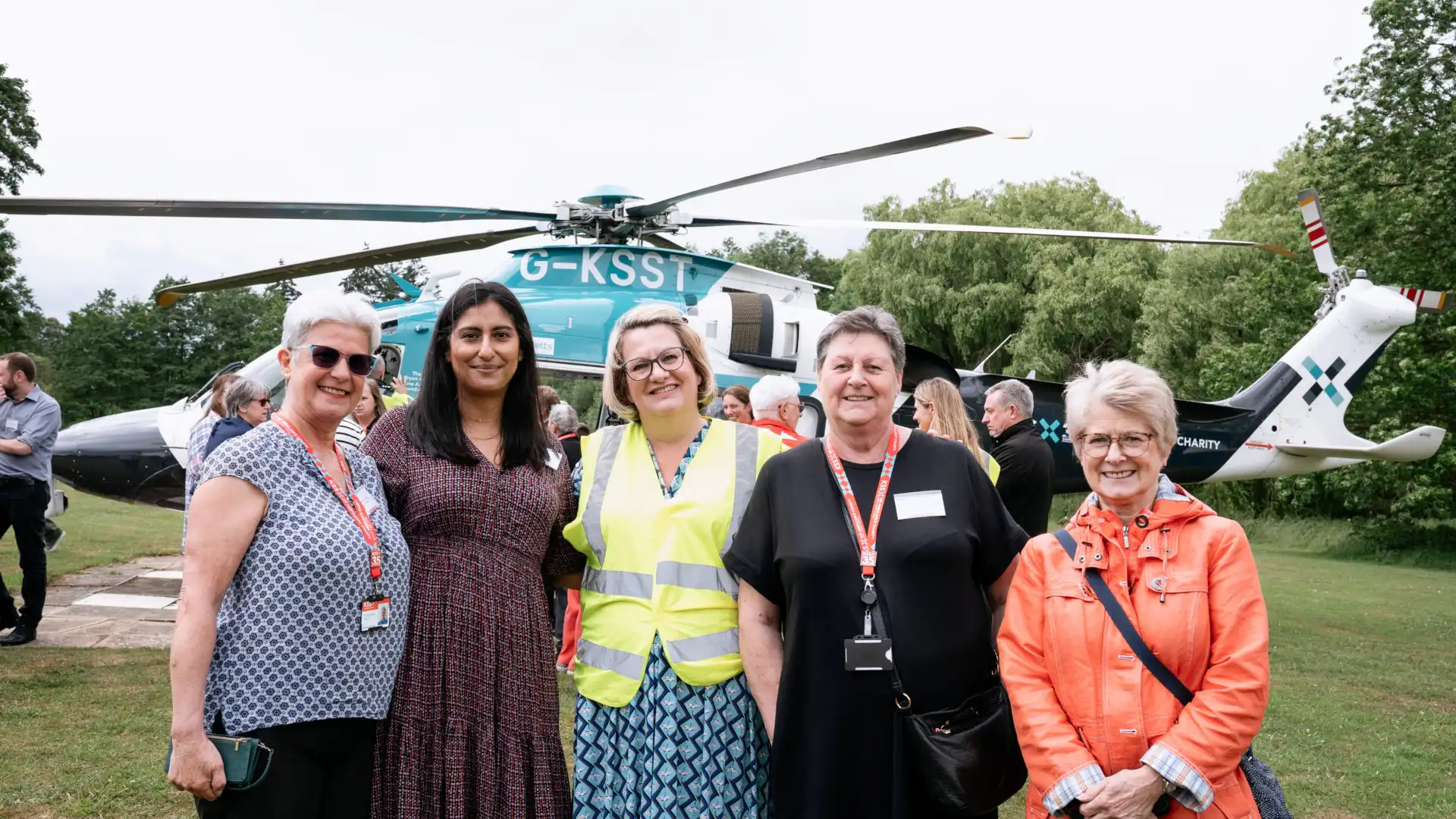 Group of five women smiling facing camera with helicopter on the ground in the background
