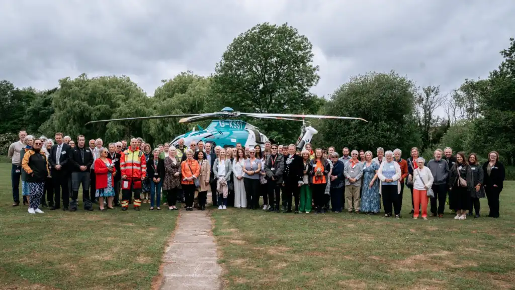 Large group of people facing camera standing in front of helicopter on ground