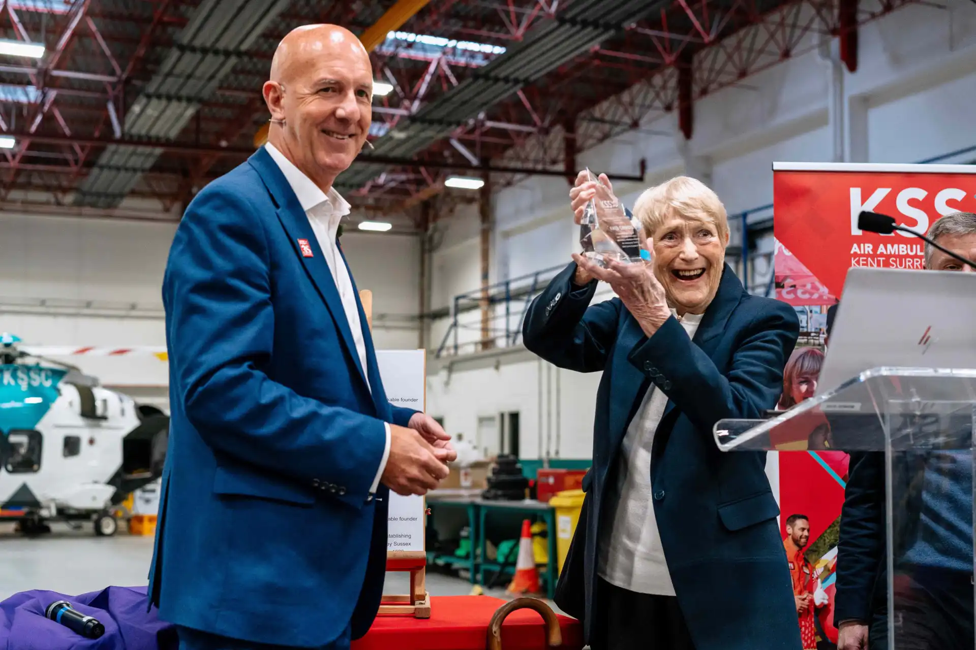Smiling lady holding award in the air next to smiling man.