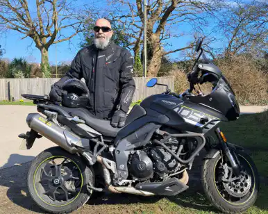 Man holding helmet standing behind motorbike
