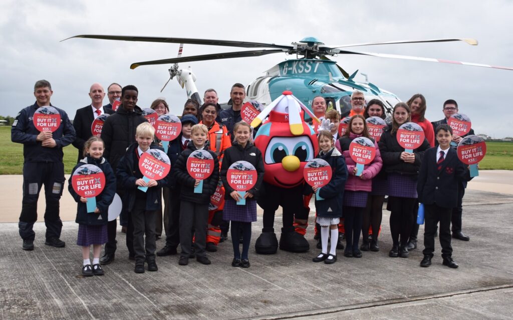 Children and young people with members of Team KSS in front of an air ambulance helicopter