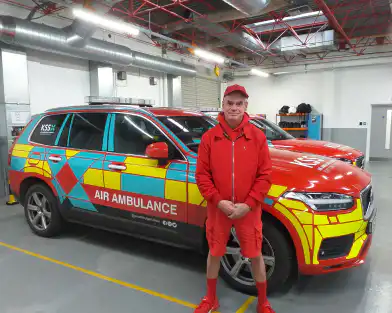 Man dressed in red looking at camera and standing in front of emergency vehicle