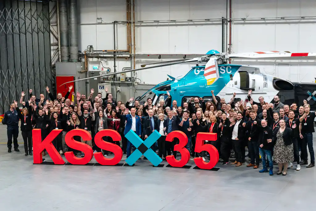 Large group of people standing in front of air ambulance helicopter in hangar looking towards camera